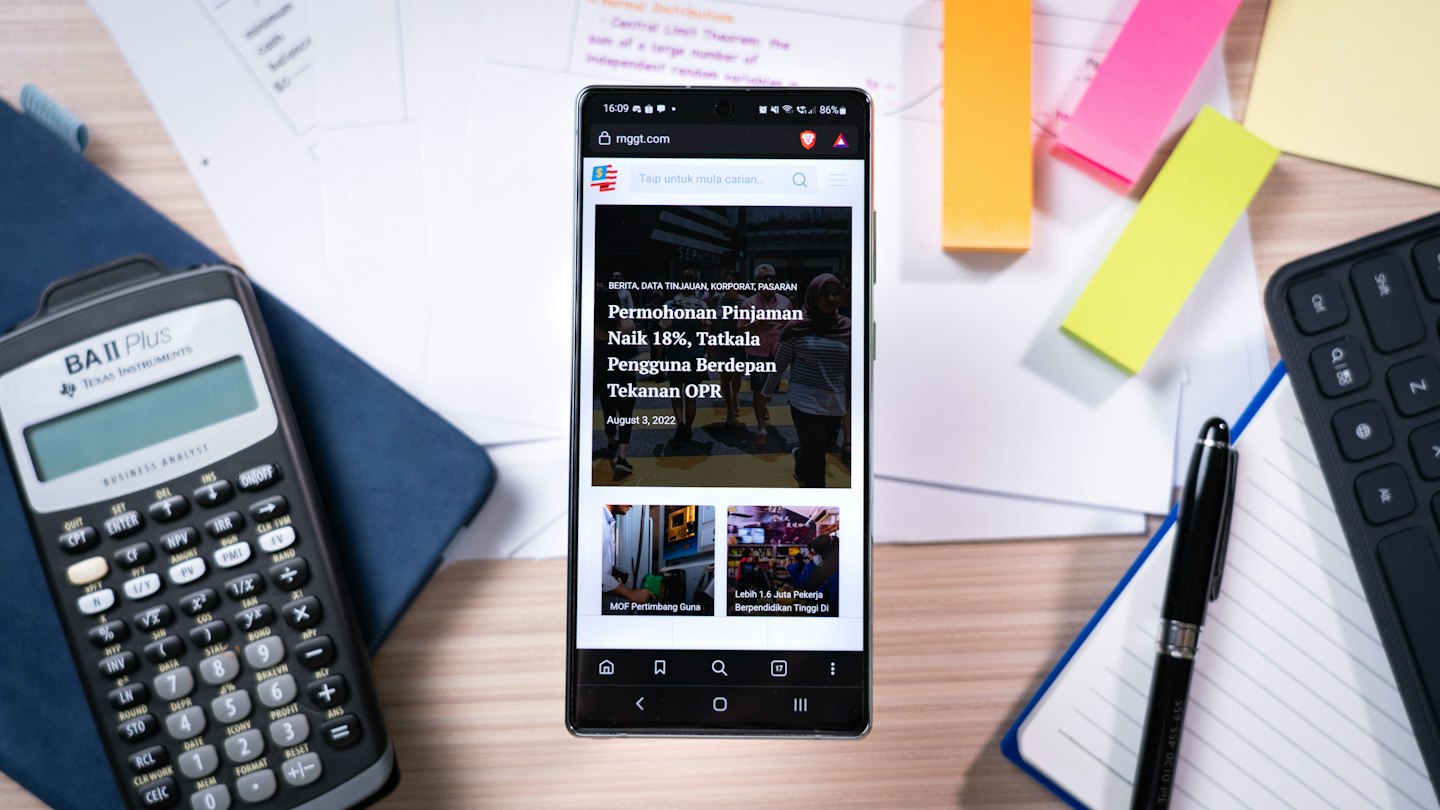 Smartphone con notizie di lavoro su una scrivania di legno con articoli per ufficio.