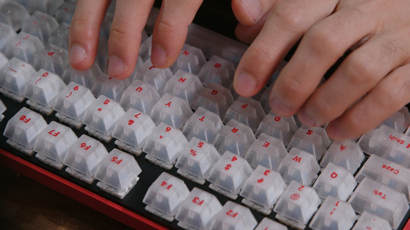 Mani che digitano su una tastiera meccanica rossa e nera con tasti bianchi.